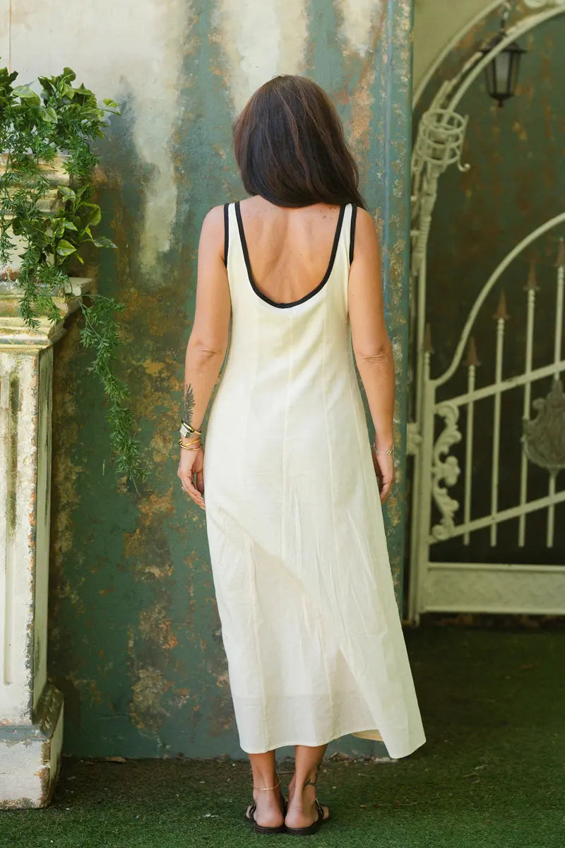Woman in a white dress standing in front of a textured wall with greenery.
