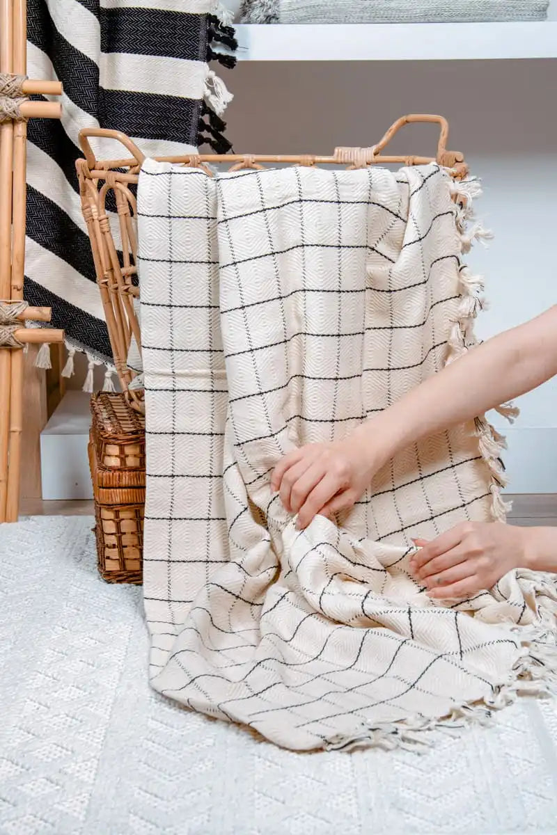 Person holding a black and white checkered blanket next to a wicker basket.
