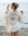 Woman on a beach holding a glass of wine, wearing a Beige Evil Eye Muslin Robe with eye design.