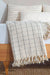 cream patterned throw blanket with tassels on a wooden surface.