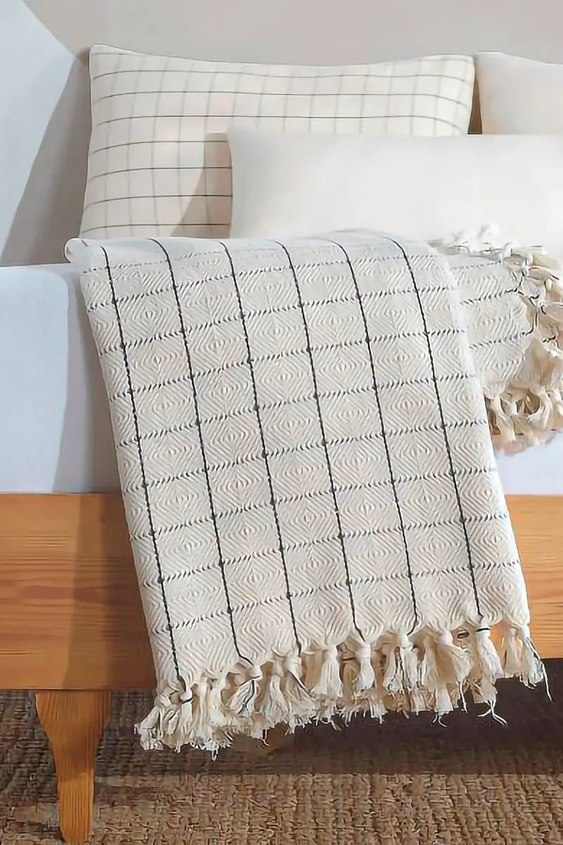 cream patterned throw blanket with tassels on a wooden surface.