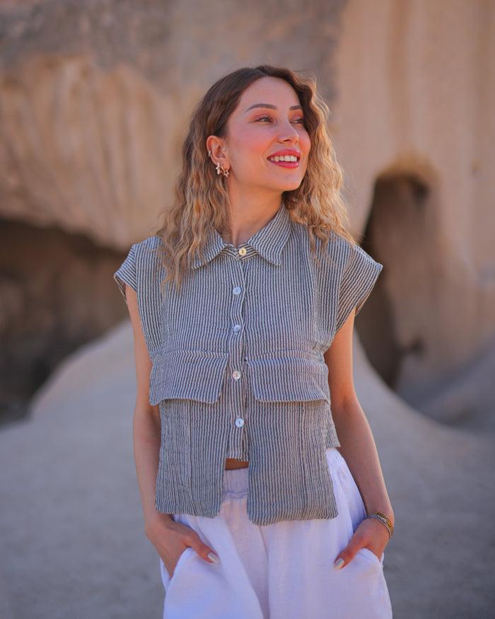 A woman standing outdoors wearing a sleeveless striped cropped shirt in a gray color.