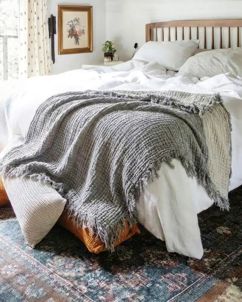 Bedroom with a bed covered in white bedding and a gray muslin throw blanket.