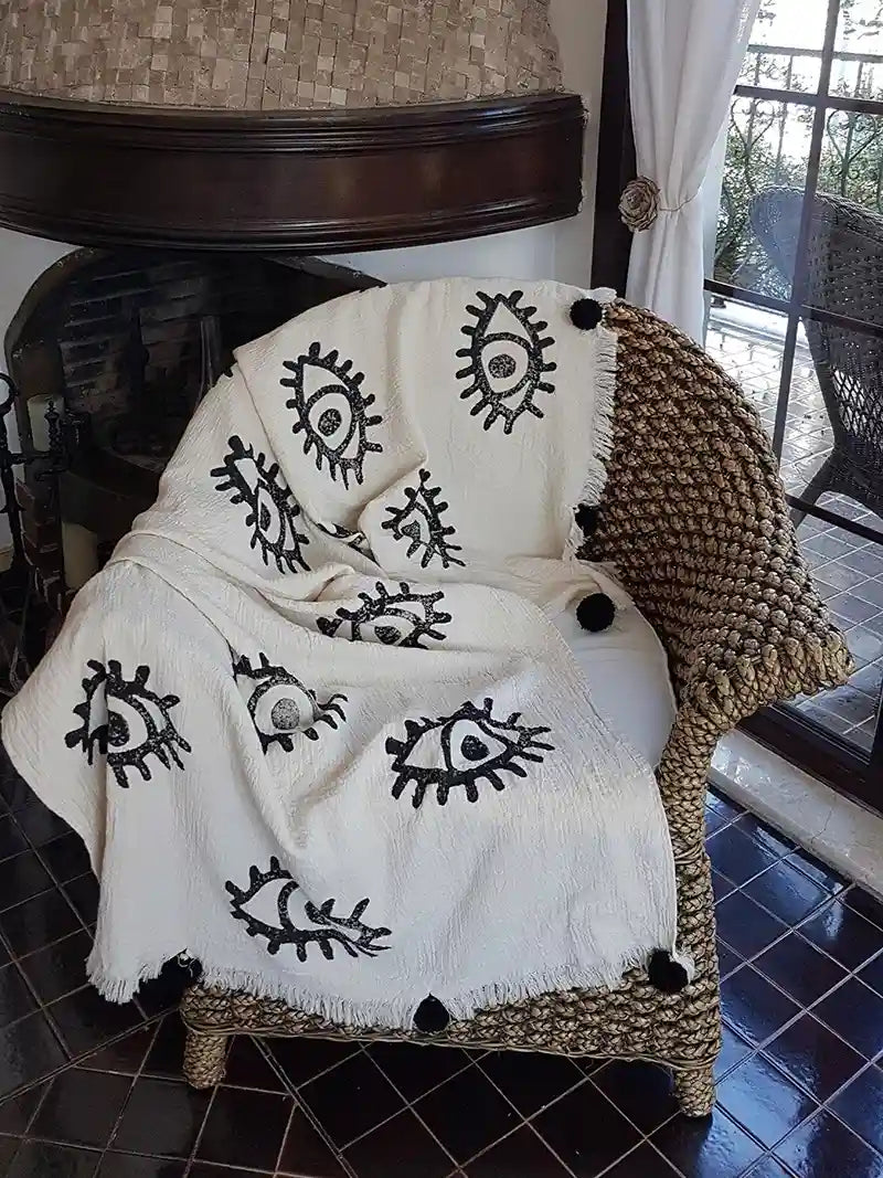 Woven chair with a white blanket featuring black eye patterns on a tiled floor.