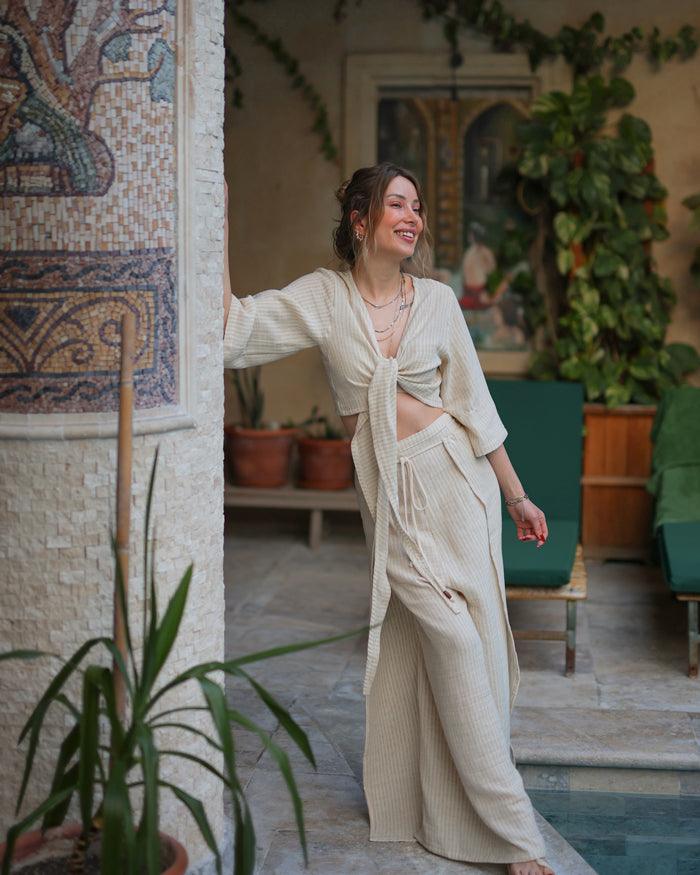 A woman in a linen deep neck front tie top stands by a pool, enjoying the sunny day.