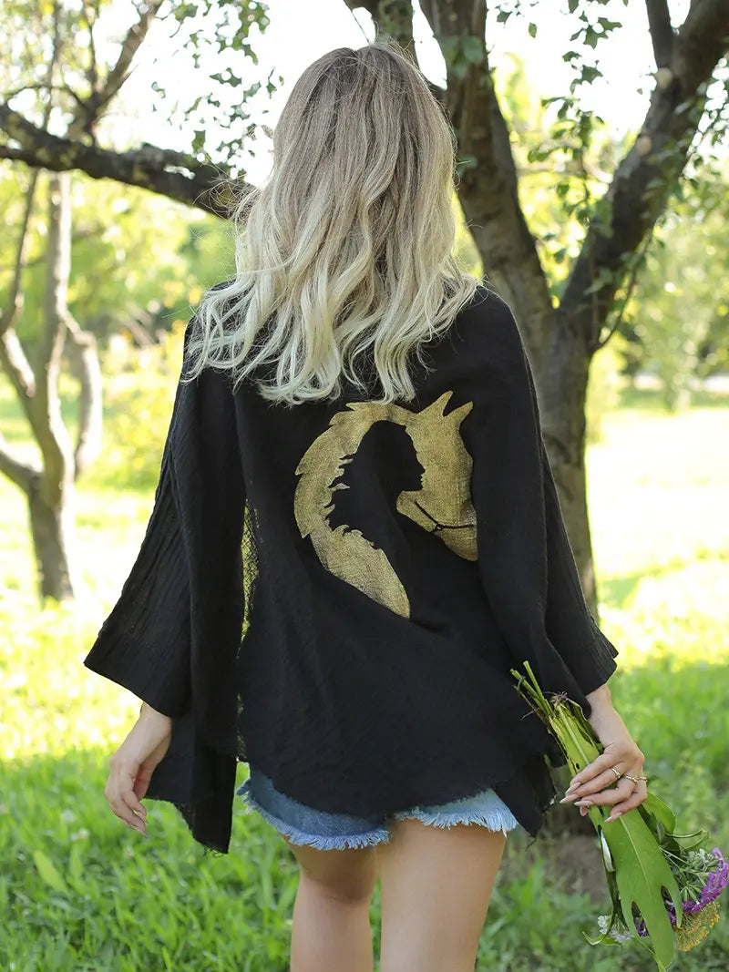 Person wearing a black kimono-style jacket with a gold horse design outdoors