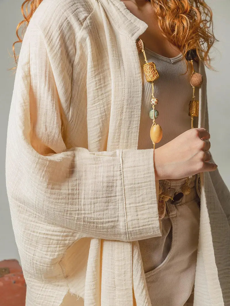 Person wearing a textured beige jacket with a necklace featuring large beads.
