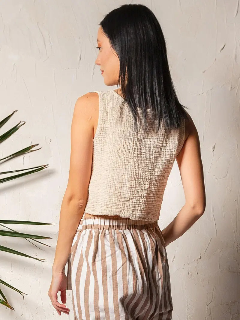 Woman wearing a beige sleeveless double gauze cotton top and striped pants against a light background