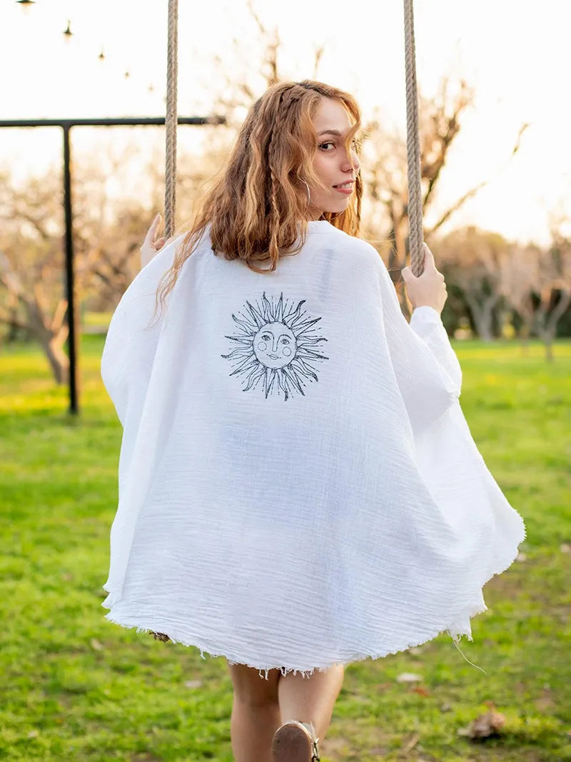 Woman on a swing wearing a white cardigan with a sun design.