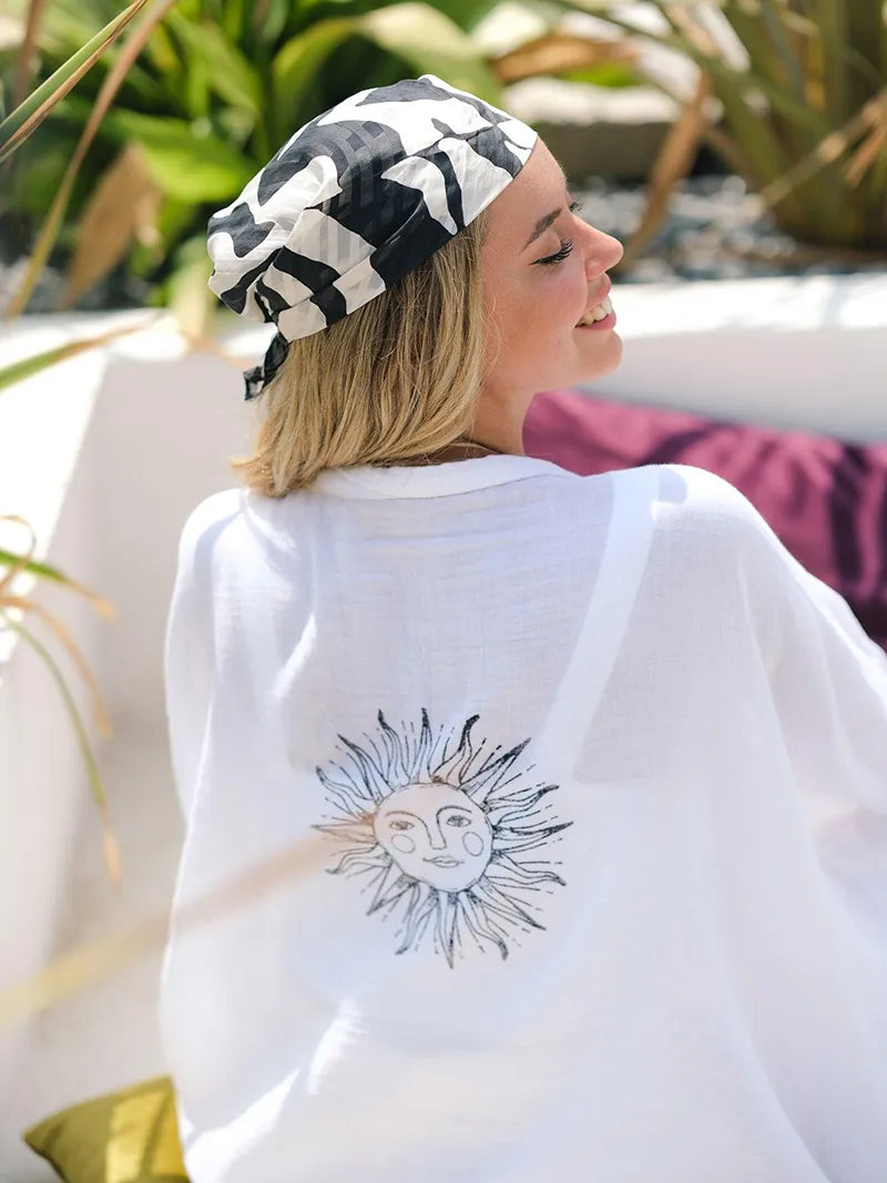 Woman wearing a white cardigan with a sun design, sitting outdoors.