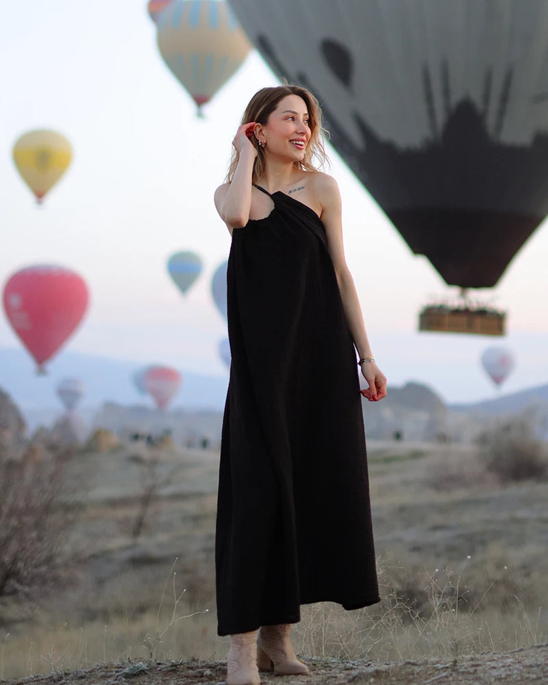 Woman in a black double gauze muslin dress standing in front of hot air balloons in a desert setting