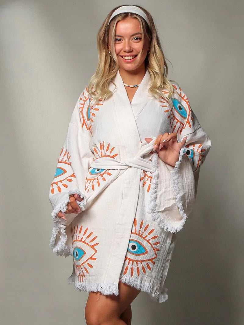 Woman wearing a white robe with eye designs on a plain background