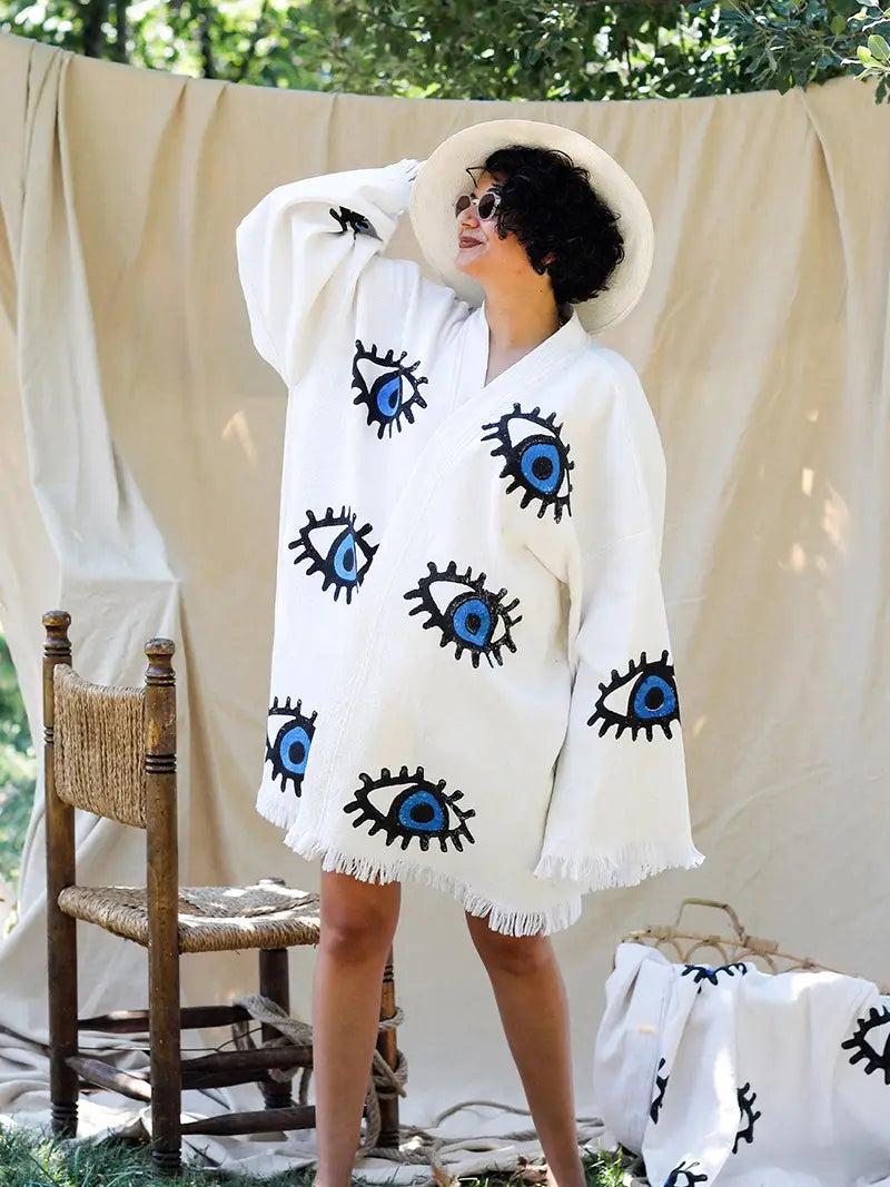 Woman wearing a white  kimono cover-up with evil eye patterns outdoors.