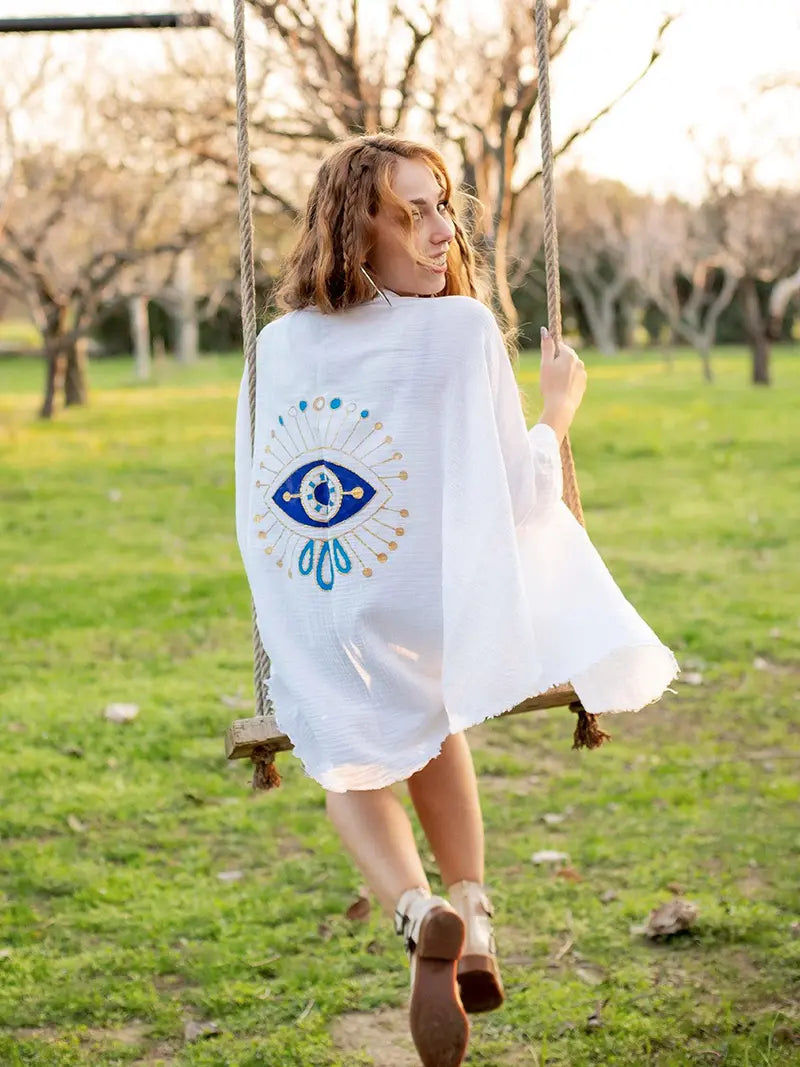 Woman in a white muslin robe with an evil eye design on a swing in a park