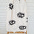 White beach towel with black evil  eye patterns on a white brick wall background