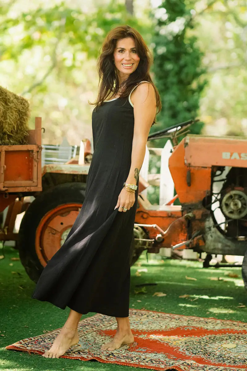 Woman in a black dress standing in front of a vintage tractor with greenery in the background