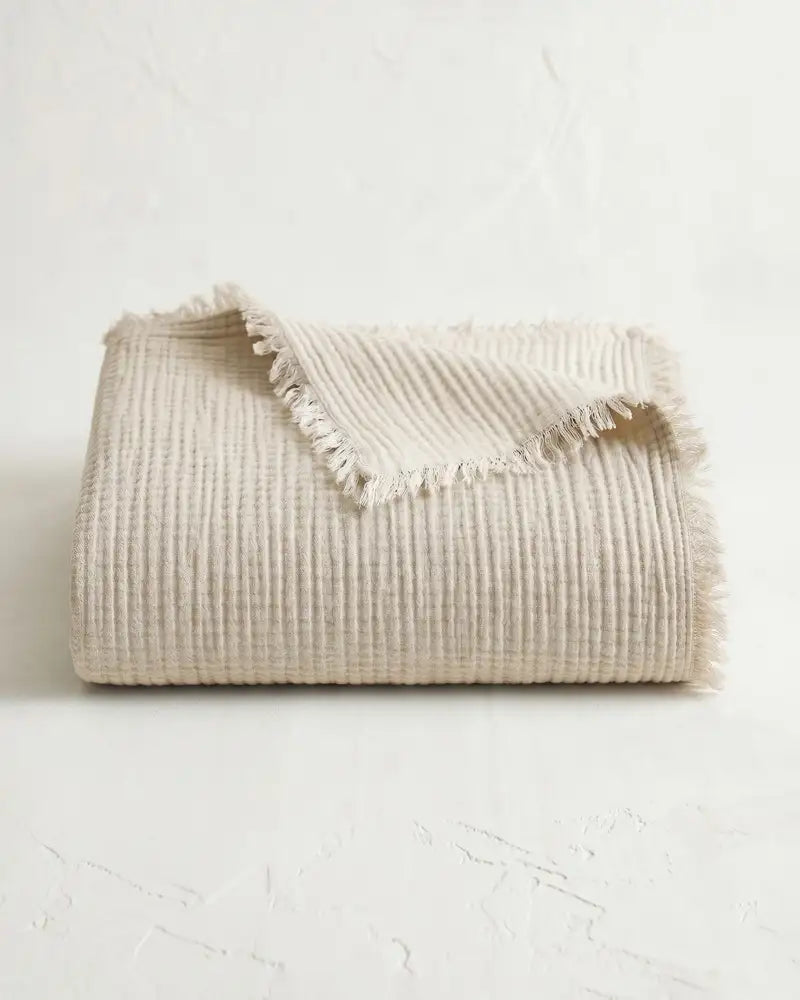 Beige crinkle gauze blanket with tassels on a white background