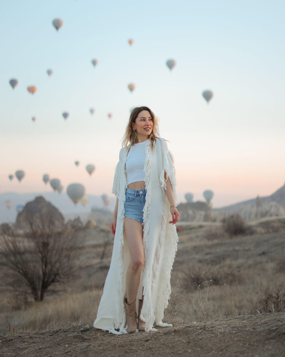 Woman with frayed long kimono robe standing in a desert with hot air balloons in the background