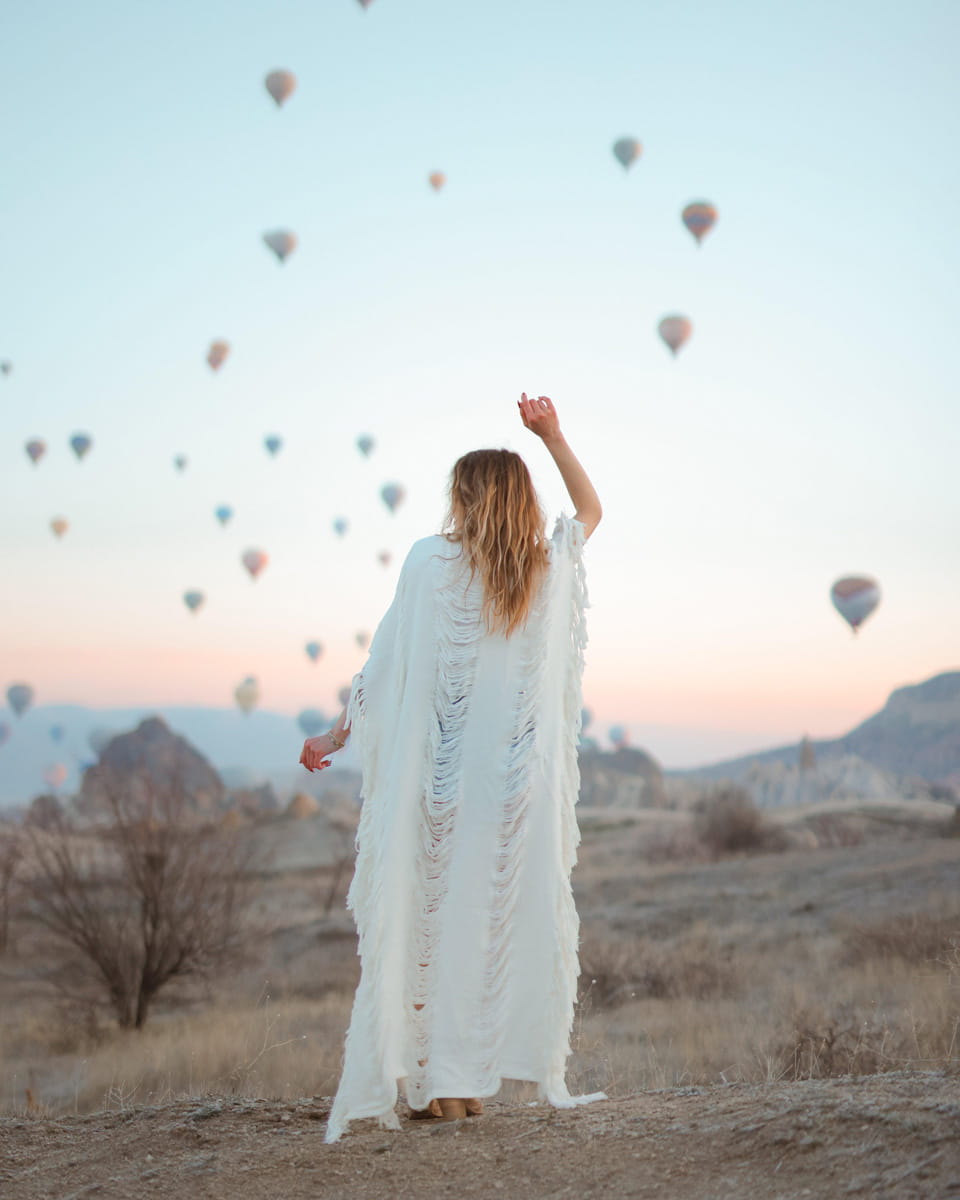 Woman in a frayed maxi kimono dress standing in a desert with hot air balloons in the sky.