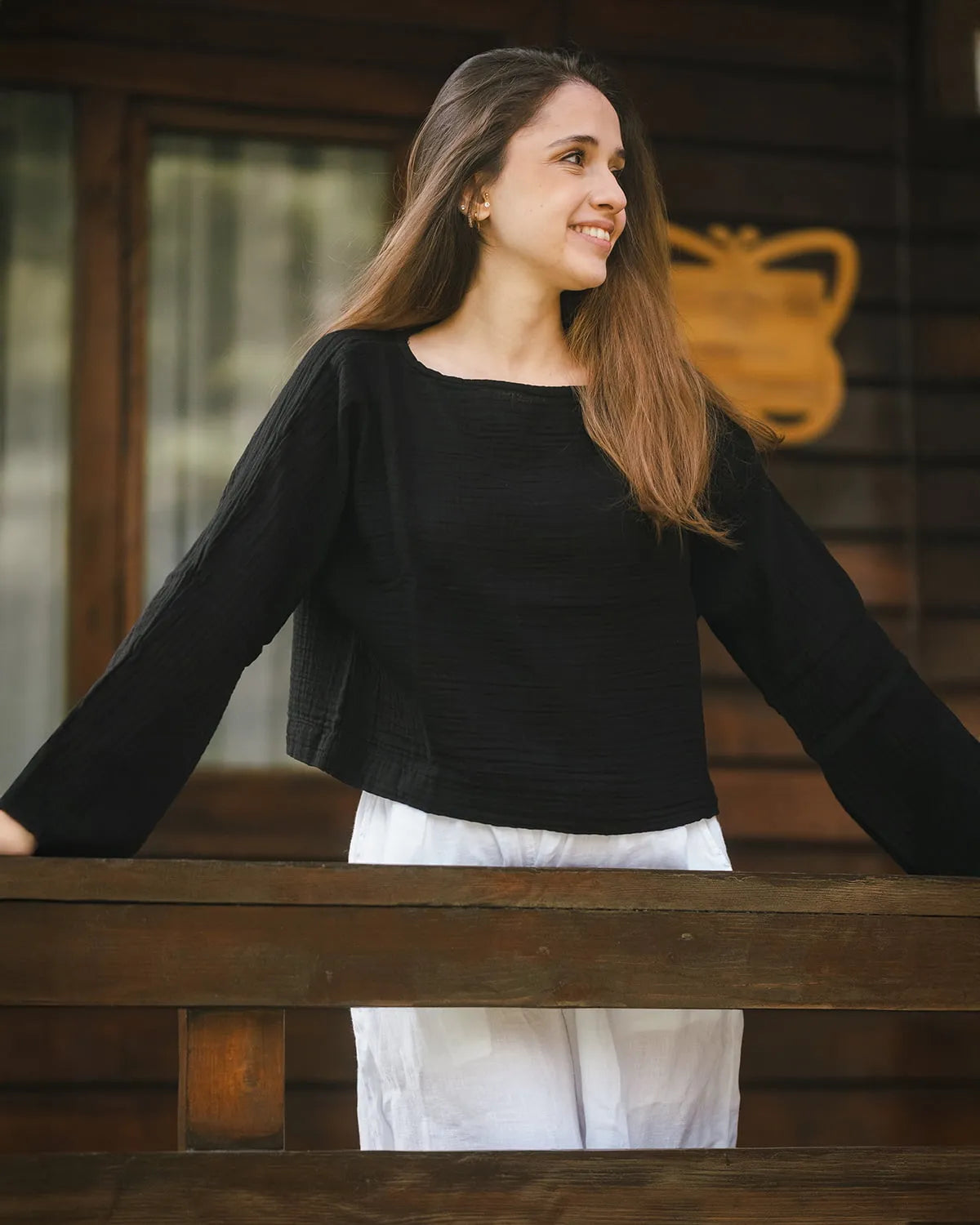 Woman wearing a black long sleeve top and white pants standing behind a wooden railing.