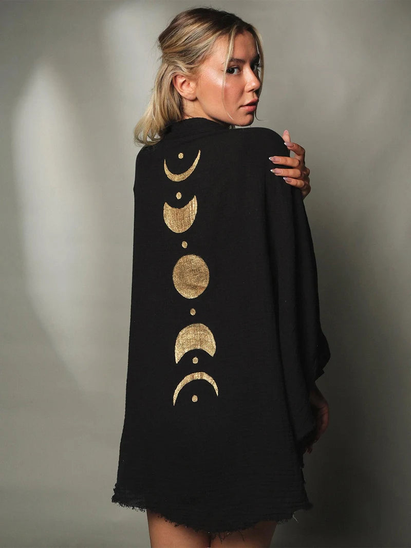 Woman wearing a black dress with gold moon phase designs on the back against a neutral background
