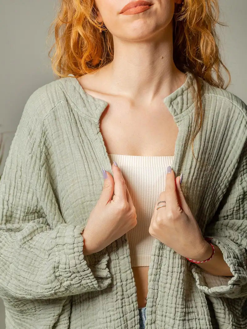 Woman wearing a textured cotton green cardigan over a white top against a neutral background