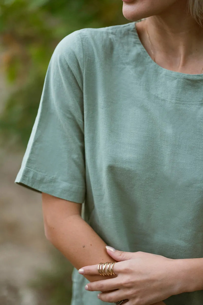 Person wearing a green t-shirt with a blurred natural background