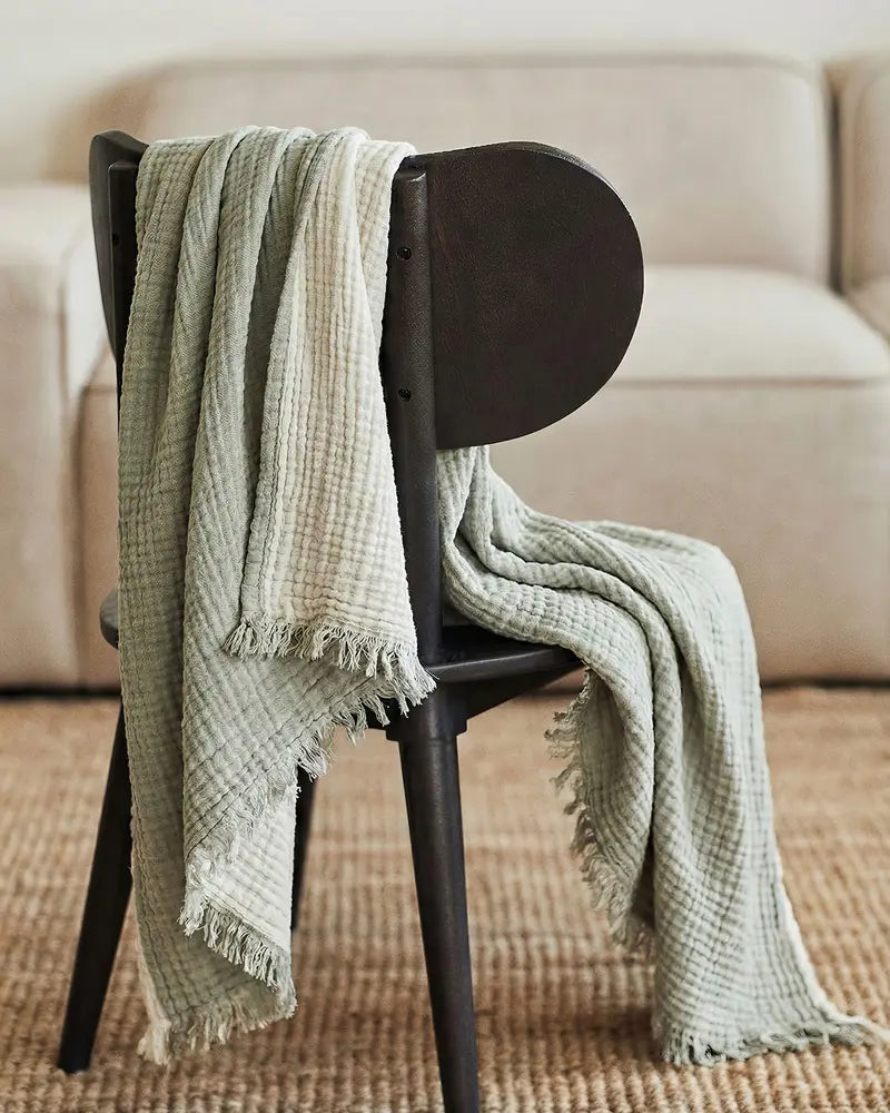 Green muslin blanket draped over a black chair in a living room setting.