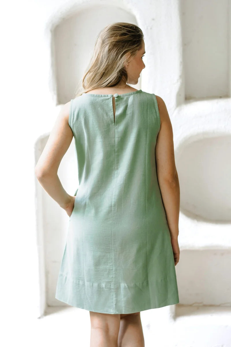 Woman wearing a light green a line mini dress in a softly lit room.