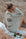 Woman sitting on a sandy beach with a glass of wine, wearing a green muslin cardigan with eye design.