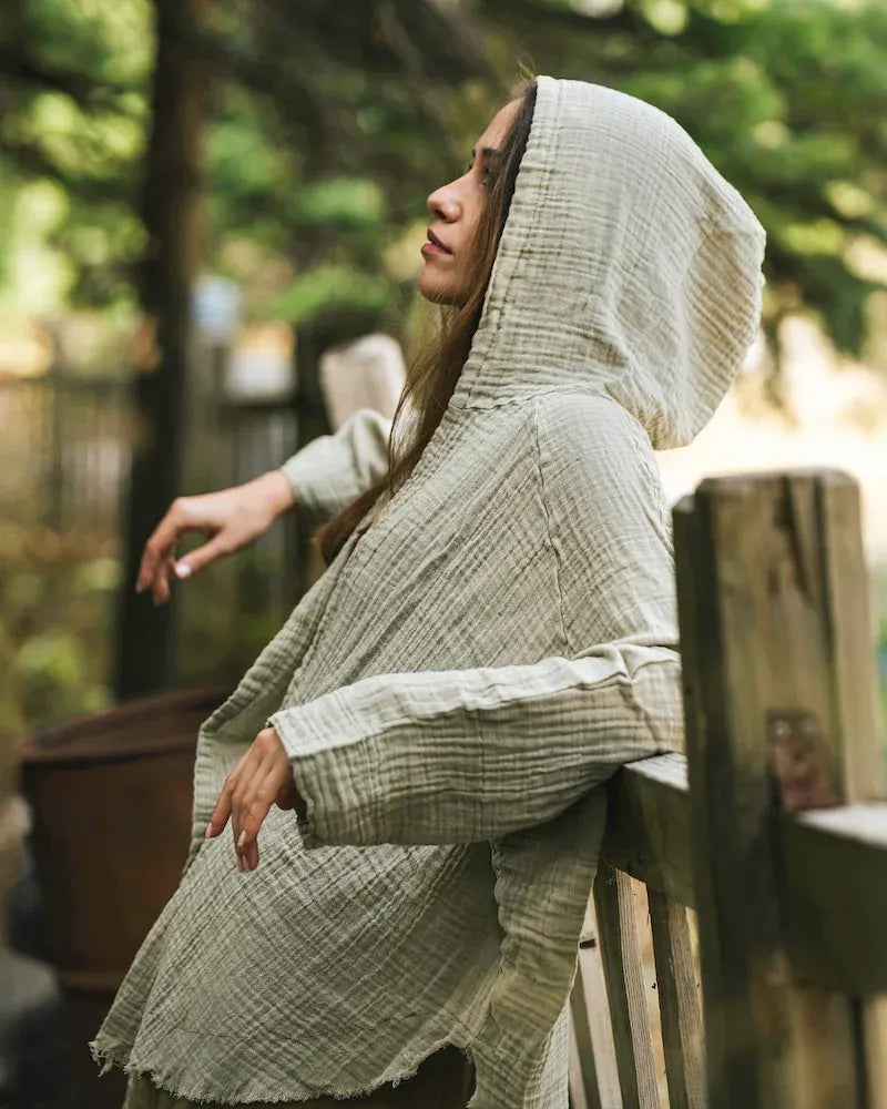 Woman wearing a crinkle cotton green hooded garment outdoors with greenery in the background
