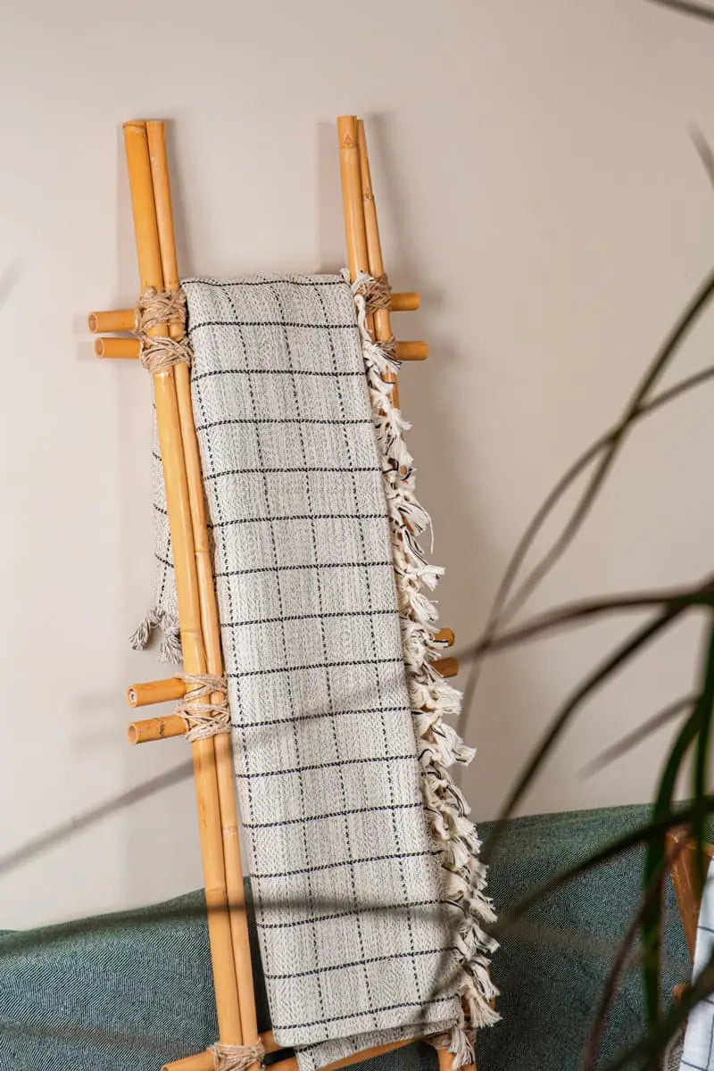 Bamboo ladder with a gray and black checkered towel draped over it against a neutral wall.