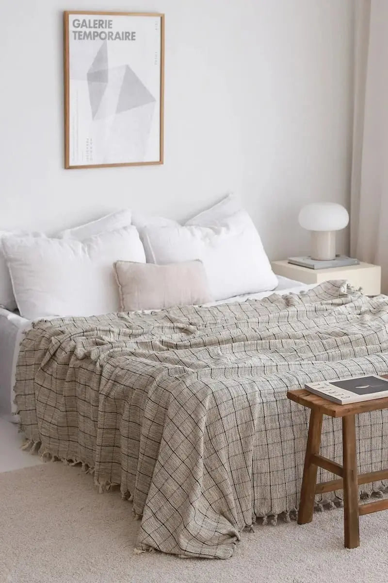 Neatly made bed with grey plaid blanket in a bedroom setting.