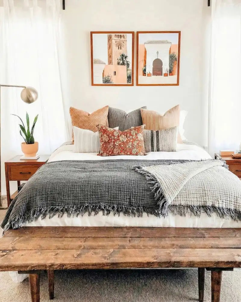 Neatly made bed with decorative pillows and a wooden bench in a bedroom setting.