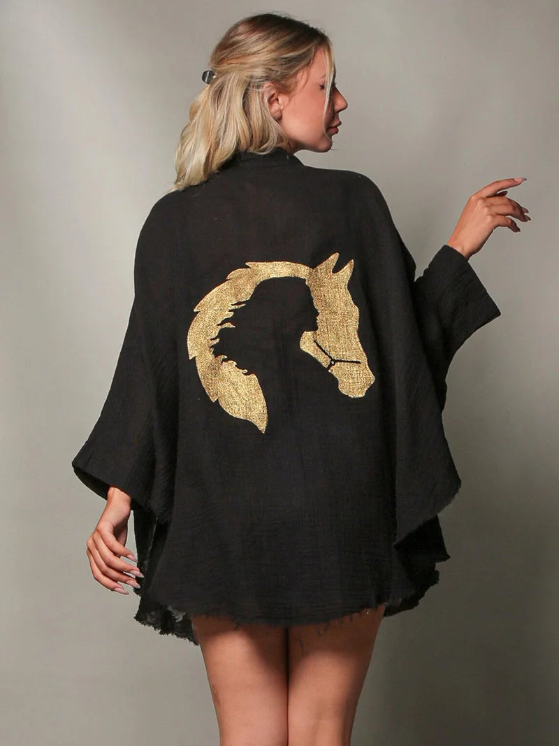 Woman wearing a black poncho with a gold horse design on a gray background