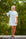 Woman wearing a white t-shirt dress standing outdoors with greenery in the background