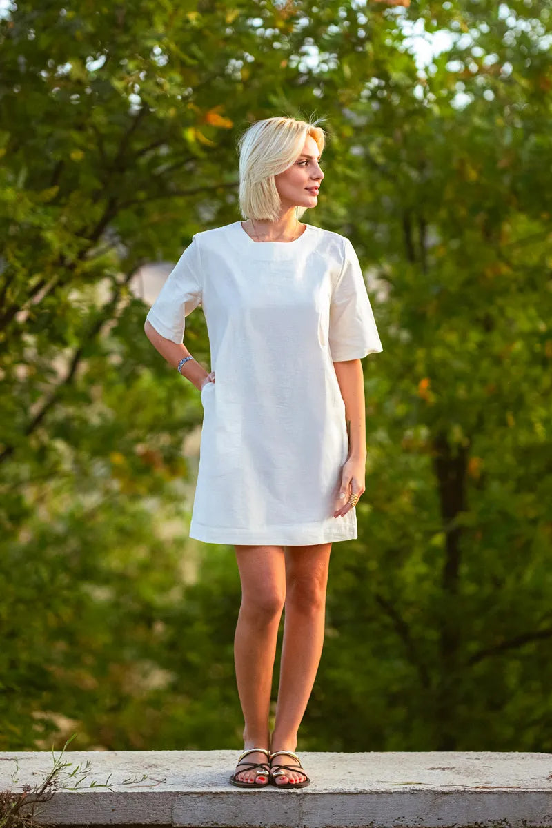 Woman wearing a white t-shirt dress standing outdoors with greenery in the background