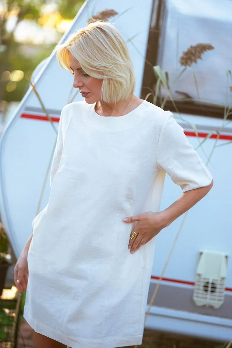 Woman wearing a white linen t-shirt dress standing in front of a sailboat.