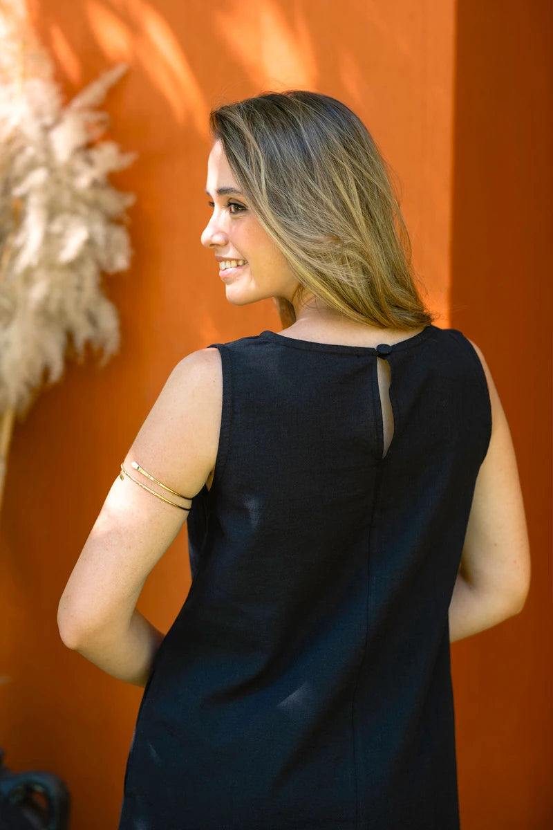 Woman wearing a black sleeveless dress against an orange wall with decorative elements.