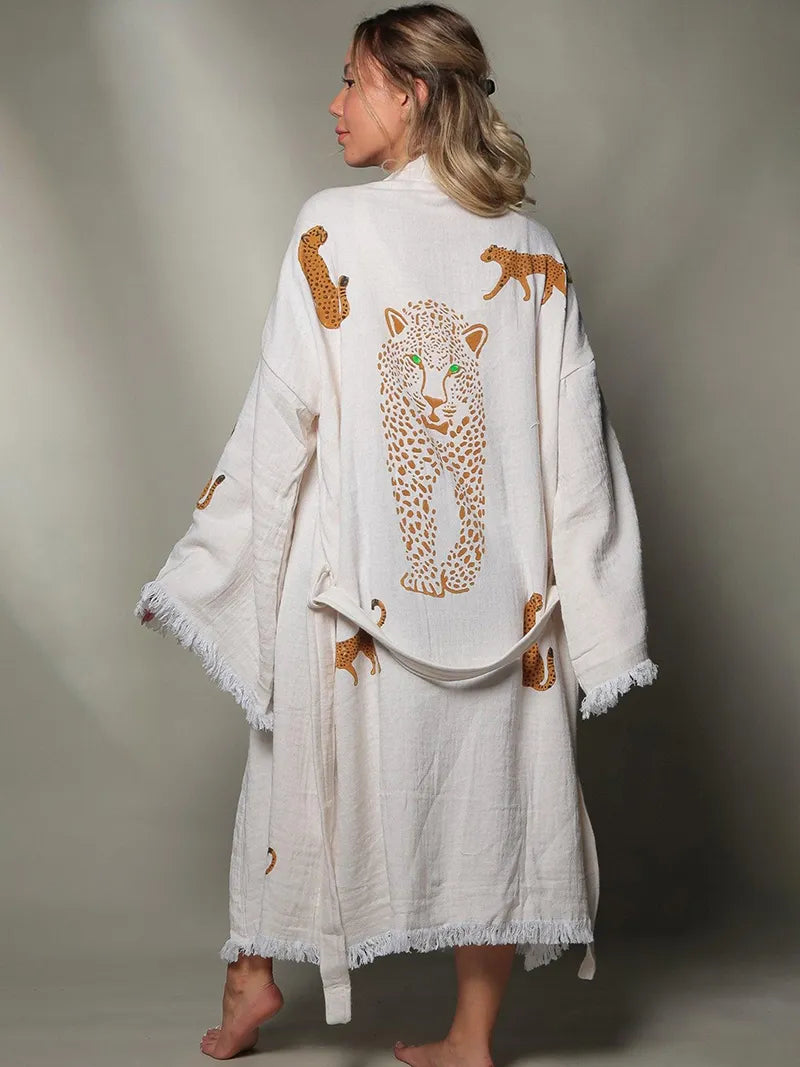 Woman wearing a white robe with leopard designs on a plain background