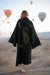 Person wearing a black coat with leopard patterns in a desert with hot air balloons in the background