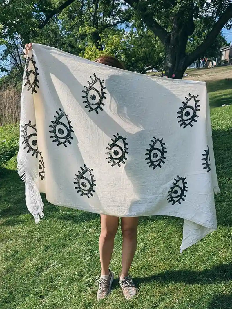 Person holding a white picnic blanket with black evil eye patterns in a park