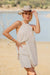 Woman in a beige outfit and hat standing on a beach with water and sky in the background