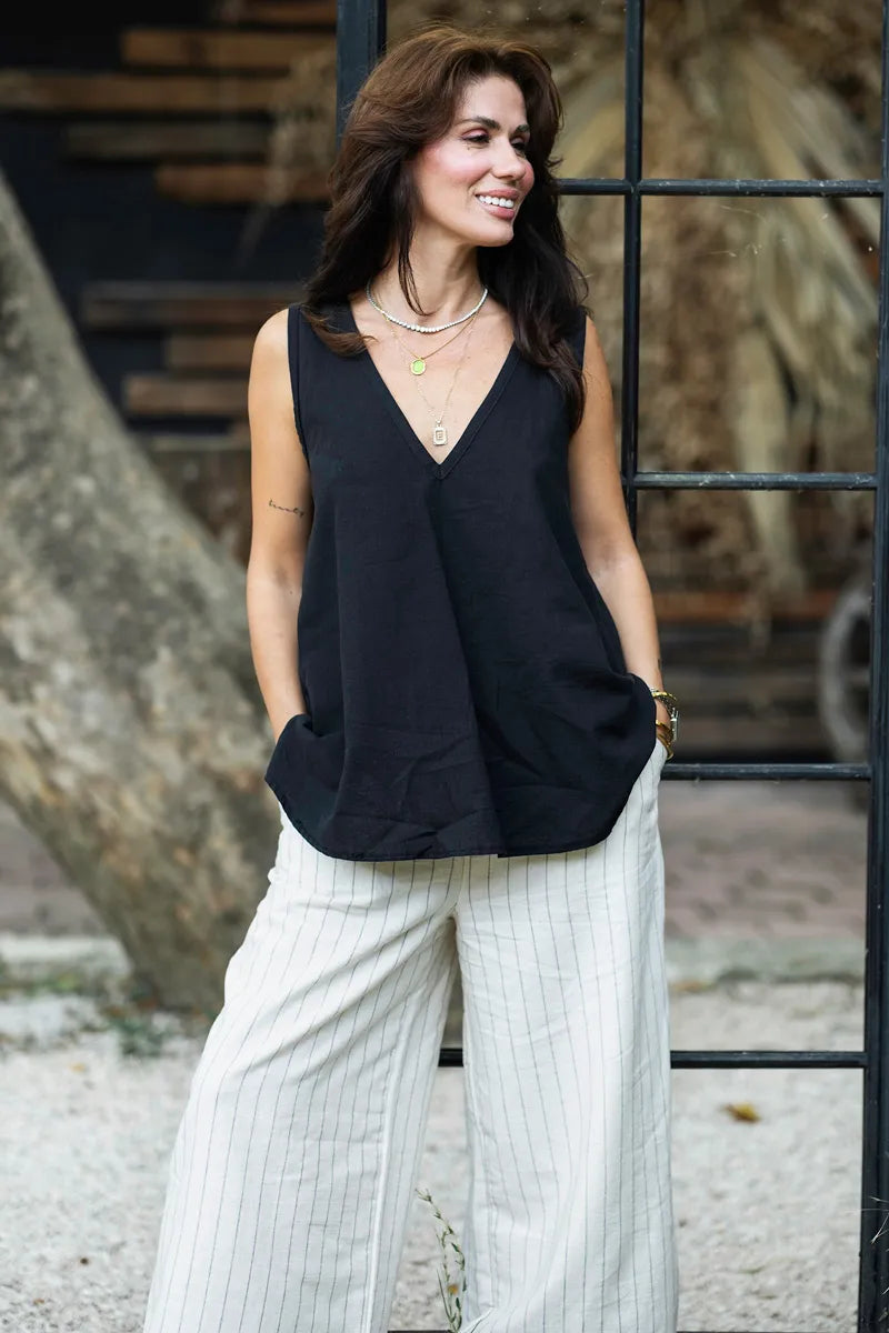 Woman wearing a black sleeveless top and linen pants standing outdoors.