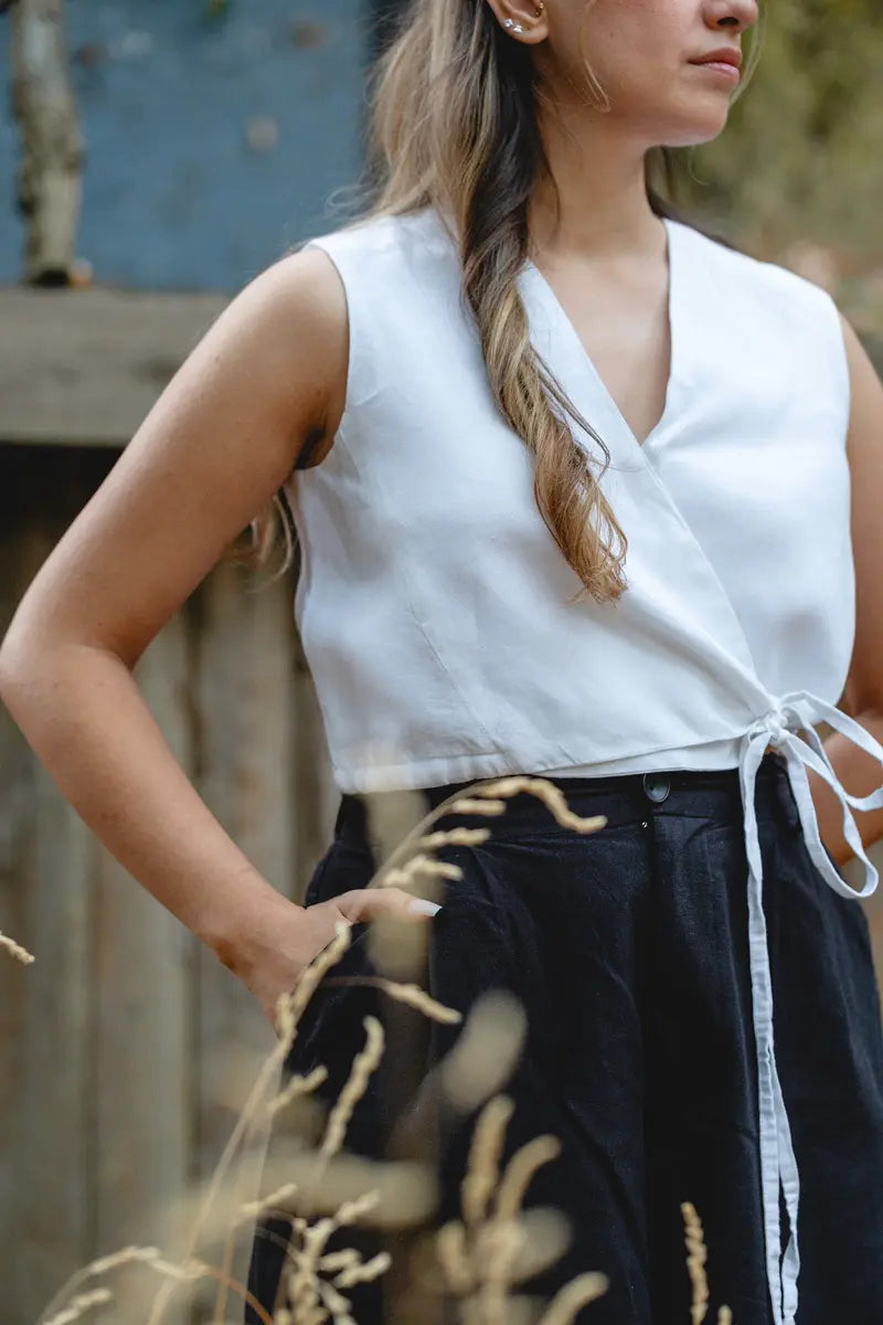 Woman wearing a white sleeveless linen vest  top with feather details and a black skirt with gold embroidery.