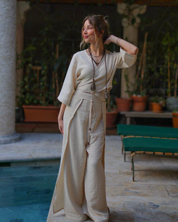 A woman in a flowing linen top stands gracefully by a shimmering pool.
