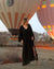A person wearing a long black kaftan dress with a crinkle texture, standing in front of hot air balloons.
