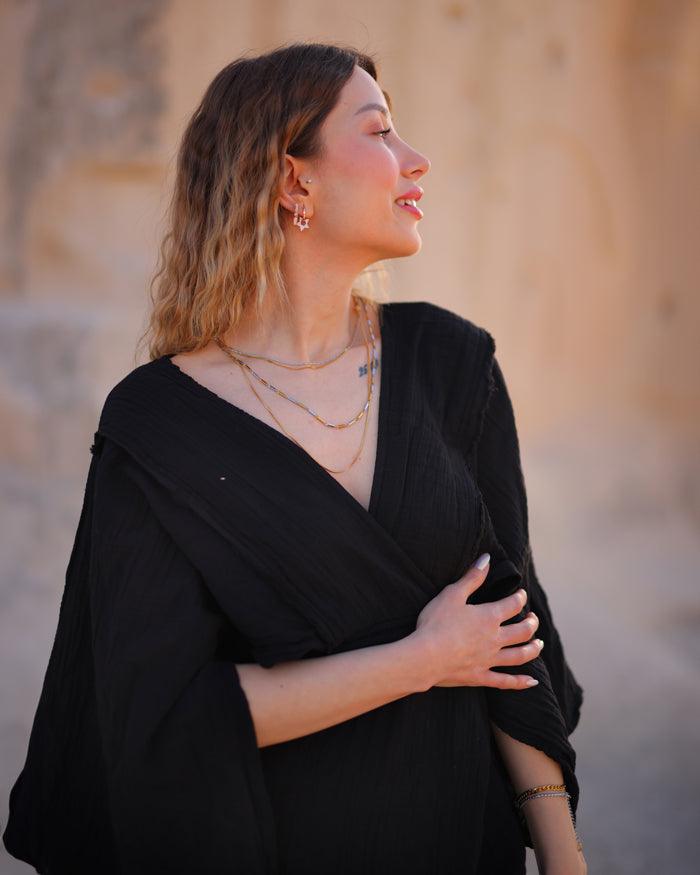 A woman wearing a flowing black summer dress poses against the backdrop of a sunlit desert.
