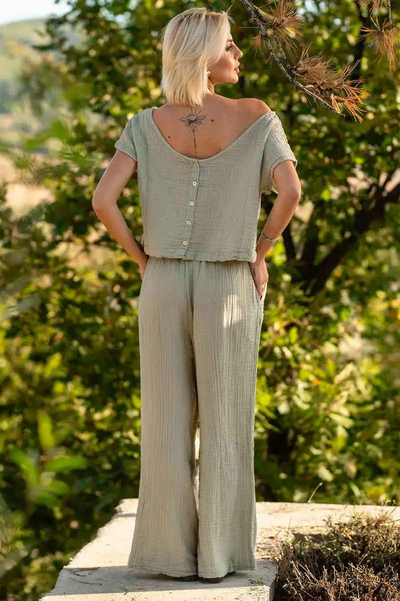 Woman wearing a light green top and green wide-leg muslin palazzo pants standing in a natural setting.