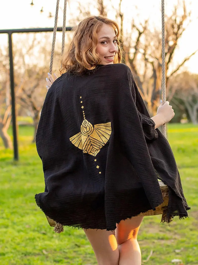 Woman in a black robe with gold mockingbird design on a swing in a park